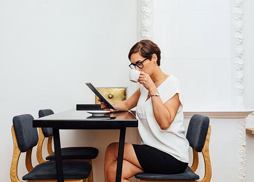 Side view of caucasian businesswoman drinking a coffee in apartment. Female entrepreneur reading from a digital tablet in her apartment at morning.