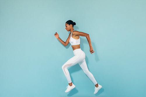 Side view of a woman running and jumping over blue background in studio