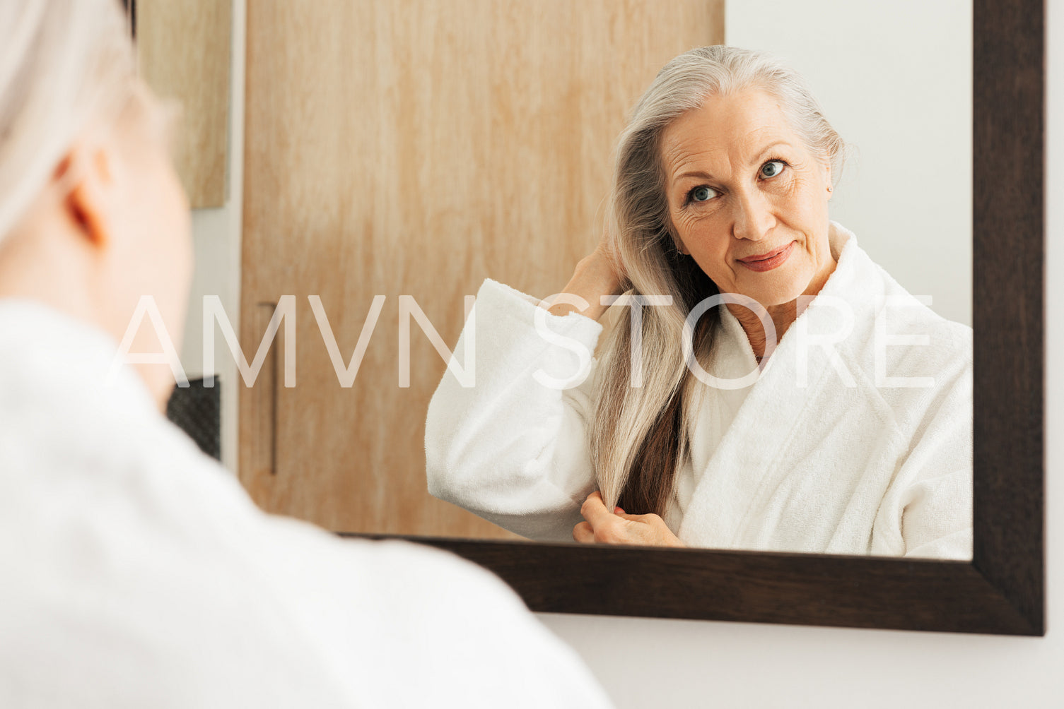 Portrait of an aged female with long grey hair looking at a bathroom mirror