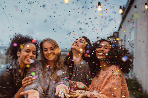 Four beautiful women standing at a terrace under confetti.