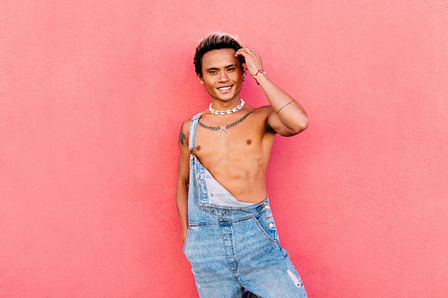 Young handsome smiling guy adjusting hair against pink wall and