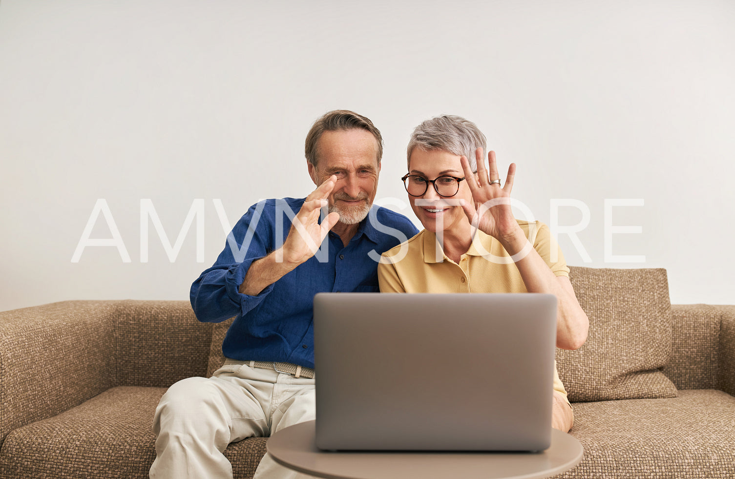 Happy senior couple waving while looking at laptop computer