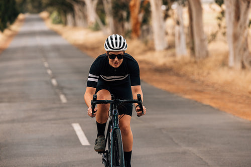 Pro bike female rider wearing helmet and sunglasses training outdoors on empty countryside road