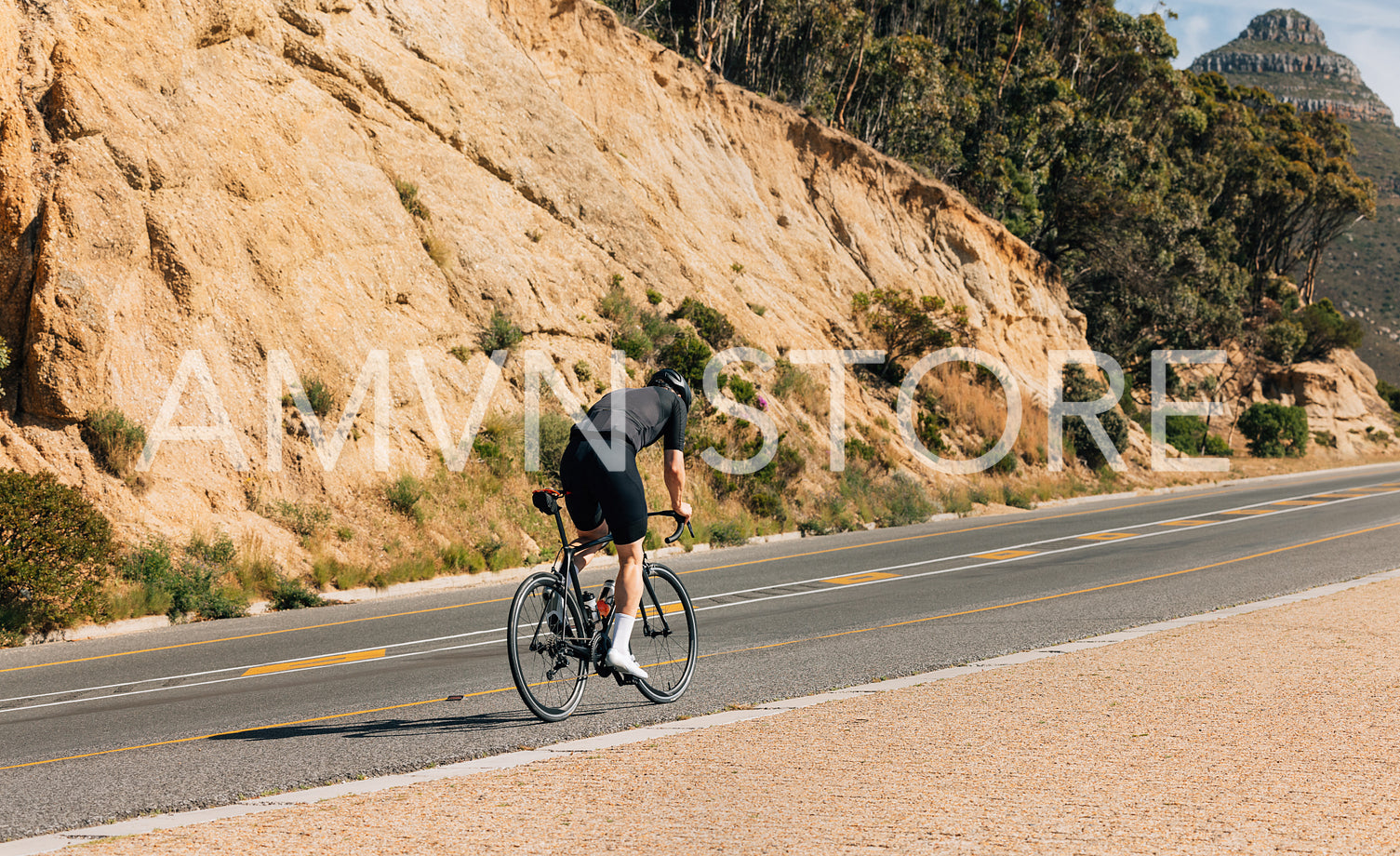 Rear view of a professional cyclist riding up on an empty road. Young male in cycling attire on a road bike.