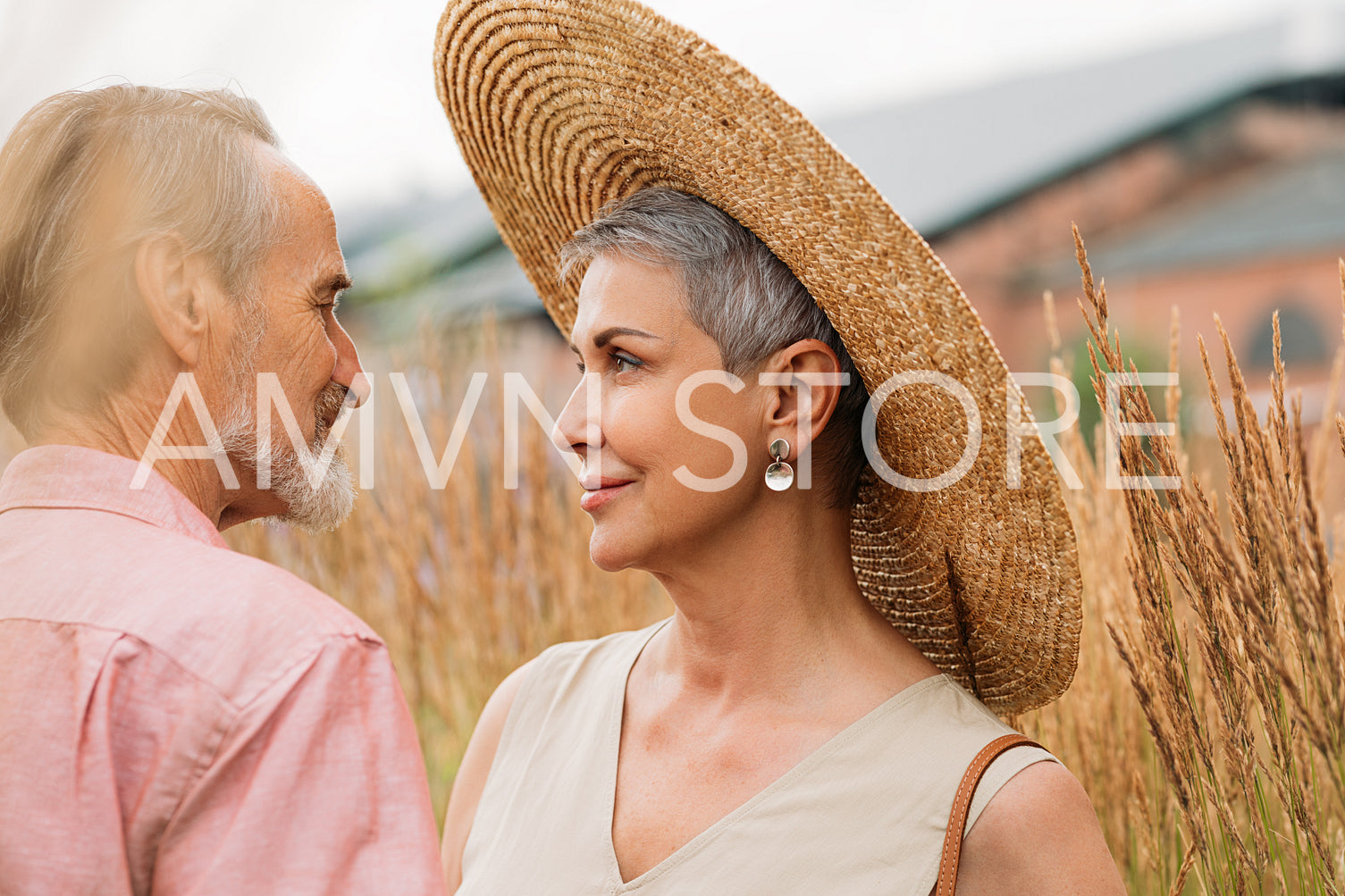 Aged woman with short gray hair wearing a straw hat looking at her husband