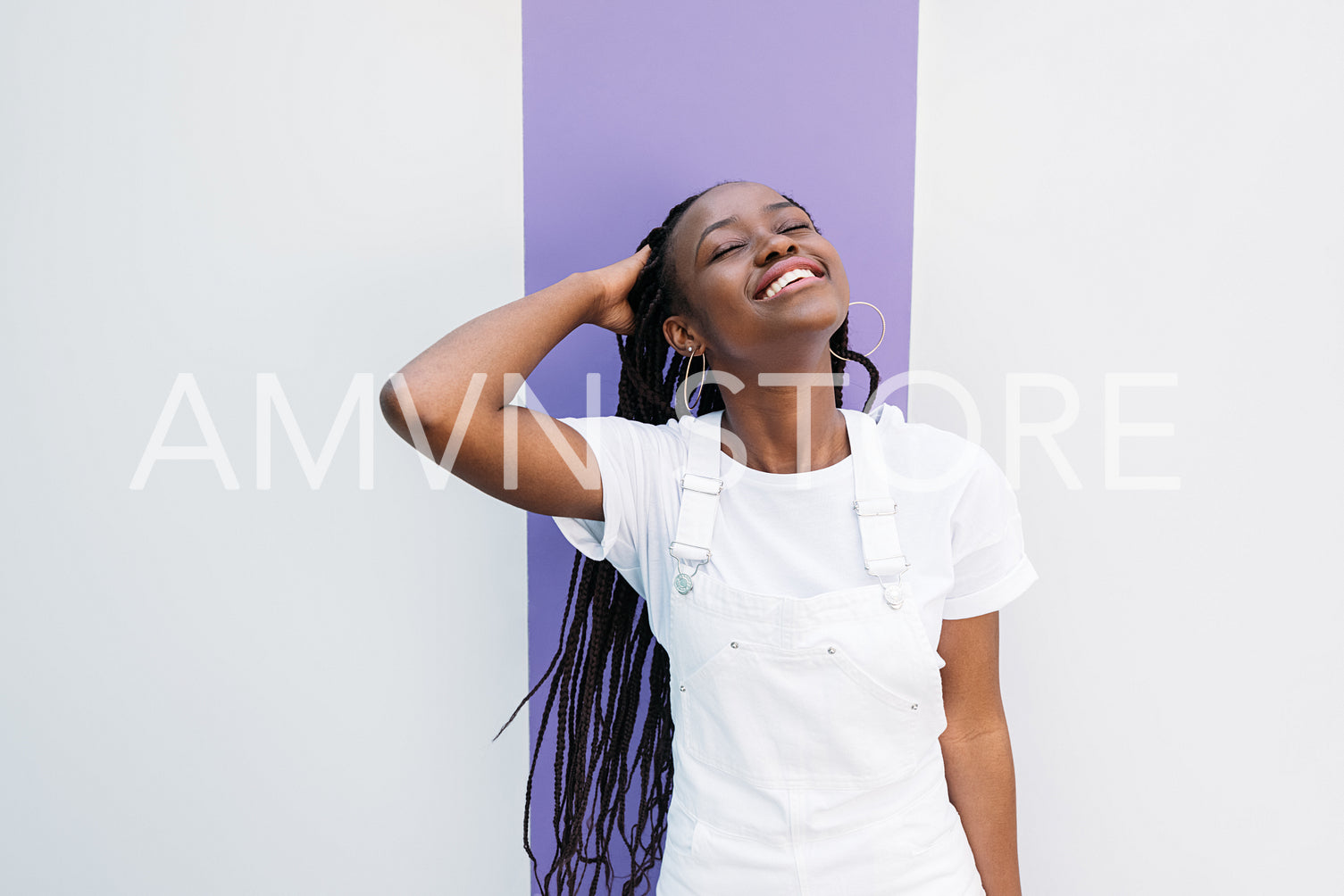 Young smiling woman in casuals adjusting hair with closed eyes against white wall with purple stripe