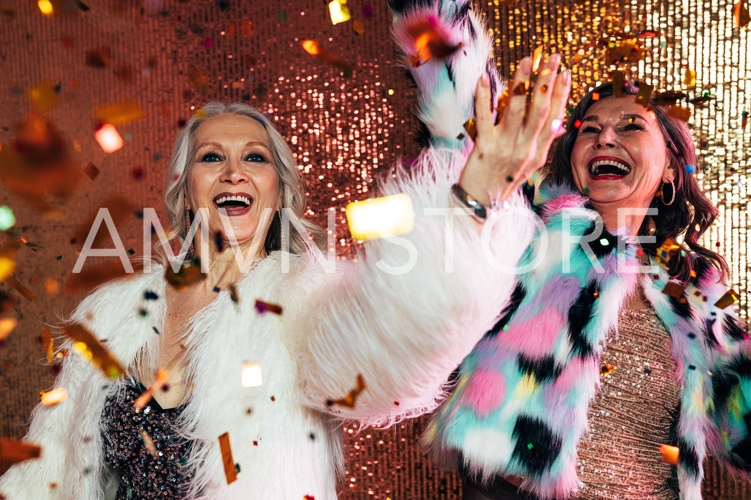 Two cheerful senior females in fur coats dancing under confetti 