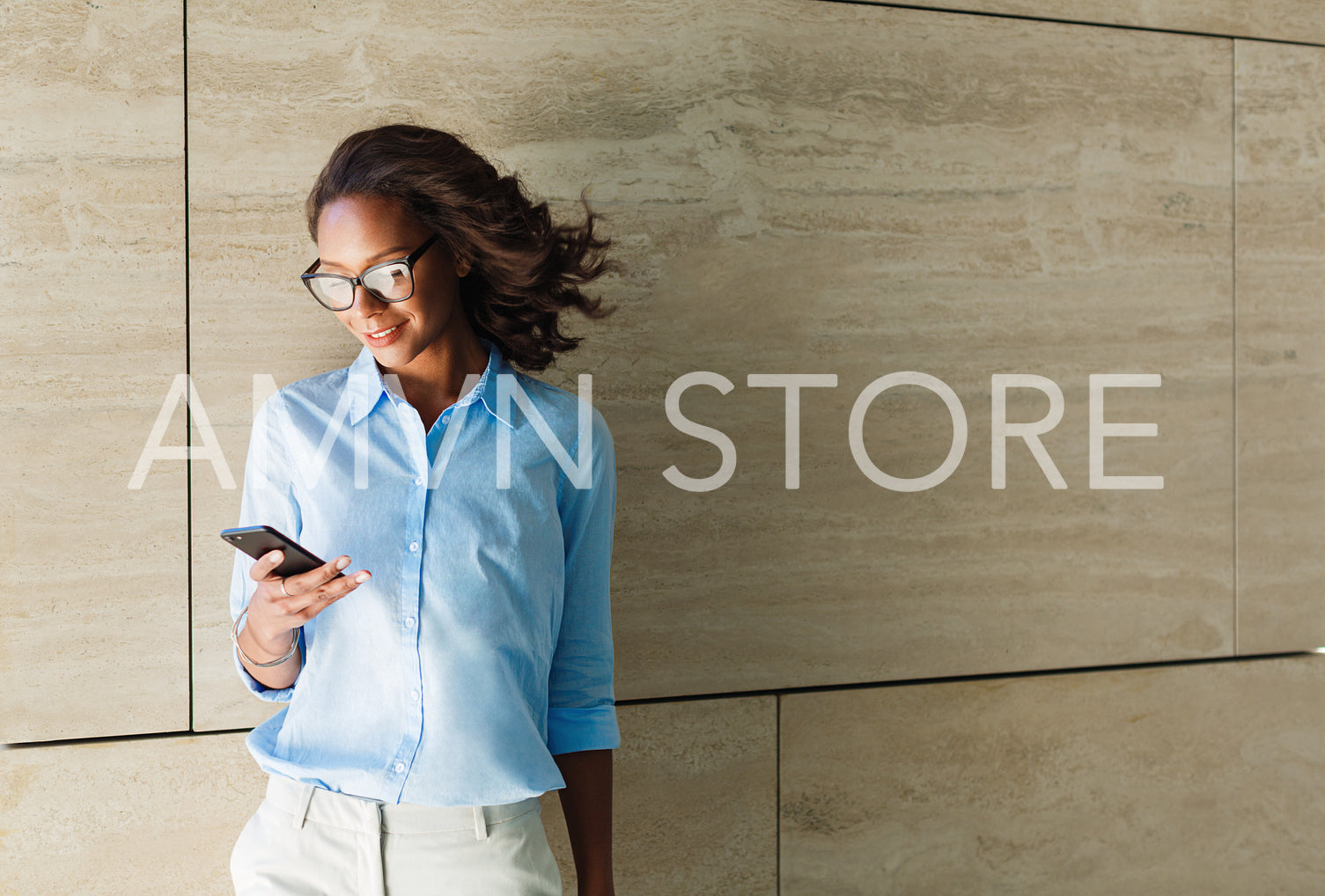 African smiling woman standing by the wall and looking at her smart phone	