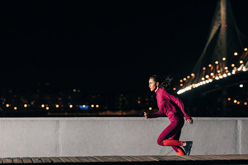 Woman runner at night. Sportswoman sprinting outdoors against a bridge.