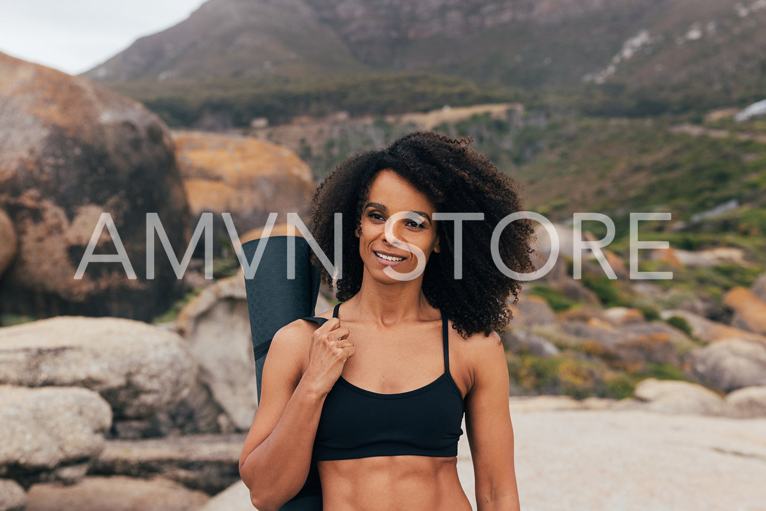 Portrait of a beautiful young woman with curly hair holding a yoga mat while standing outdoors