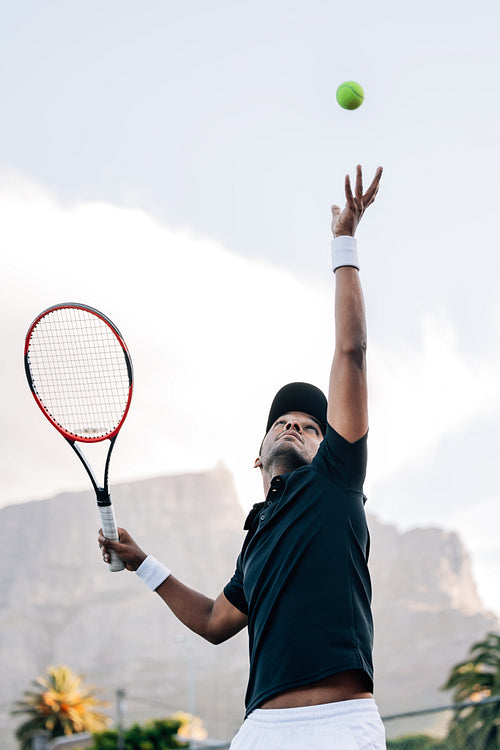 Tennis player throwing a ball in the air hitting a serve. Player is serving the ball in a match.