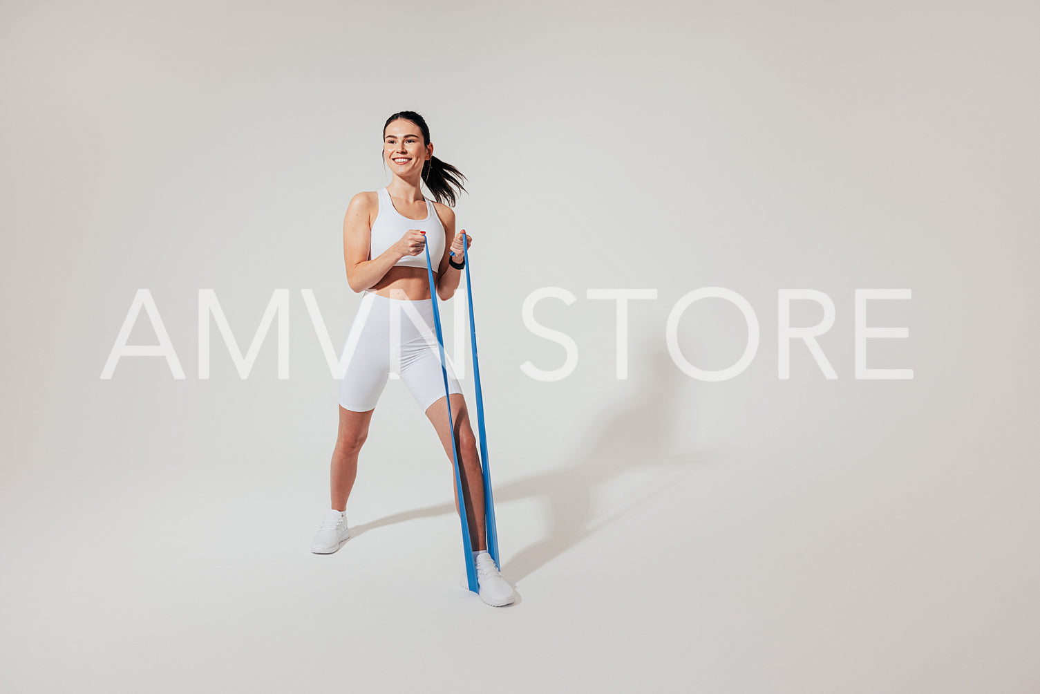 Positive woman in white fitness attire warming up her arms with a resistance band