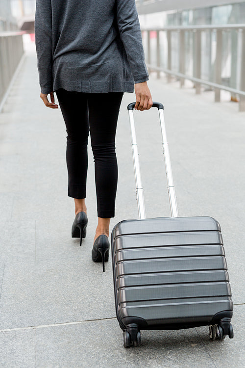 Unrecognizable businesswoman pulling suitcase inside of airport terminal