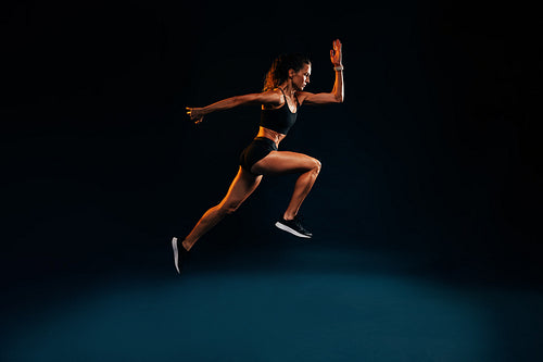 Fit woman running and jumping in the studio. Young female sprinting against dark background.