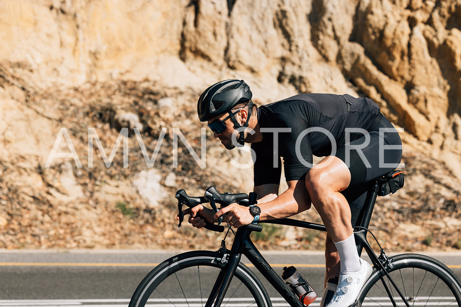 Professional road bike rider in black sportswear. Side view of a young male riding bicycle against a mountain.