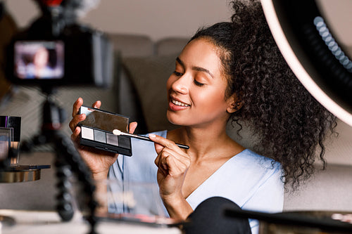 Beautiful woman holding a makeup palette while recording video at home