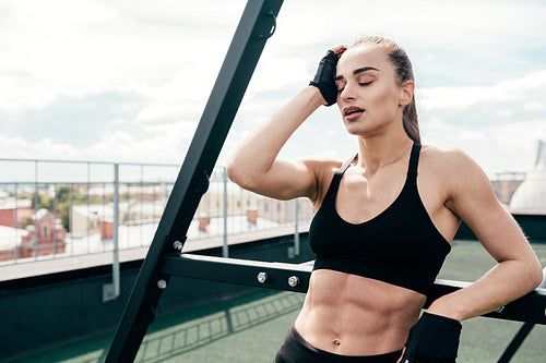 Tired woman having rest after workout on a terrace at power rack