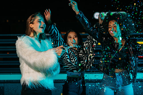 Three girlfriends having fun on roof with champagne an confetti