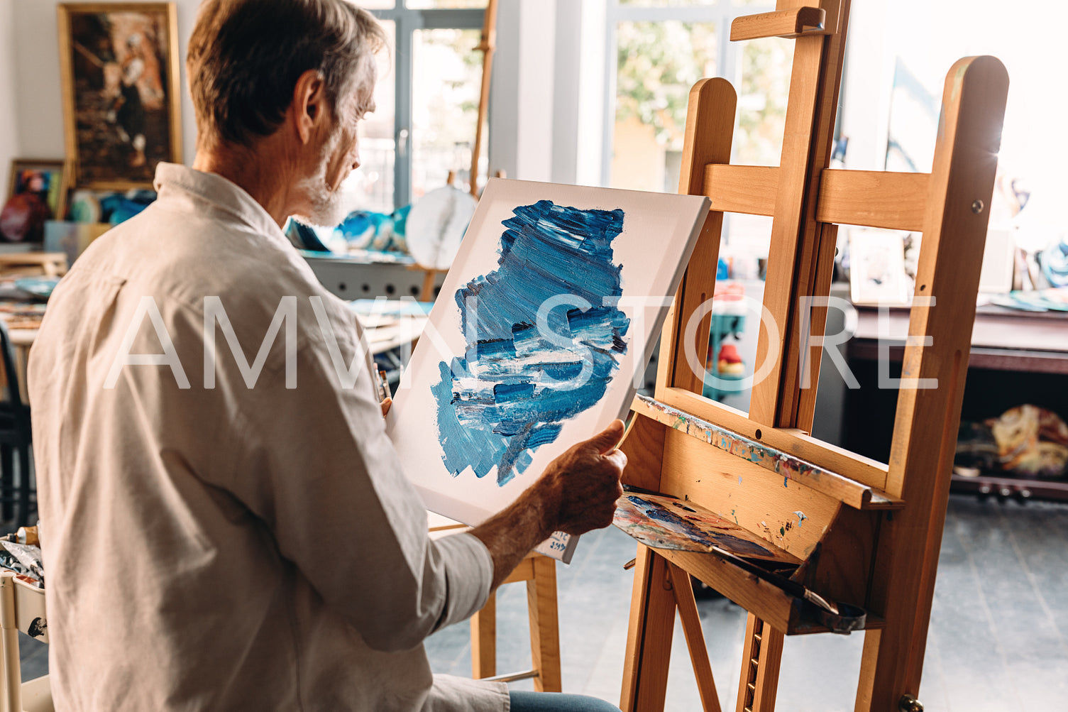 Back view of male painter holding a canvas with abstract picture sitting at easel	