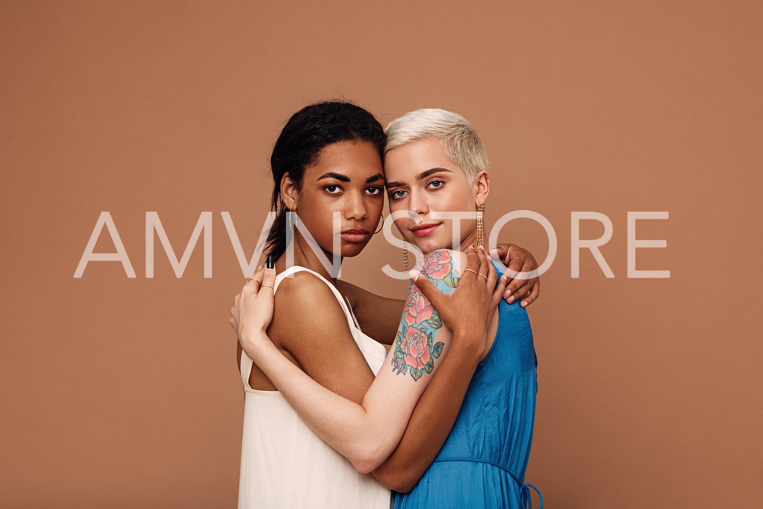 Two beautiful women embracing in the studio. Females in dresses looking at camera