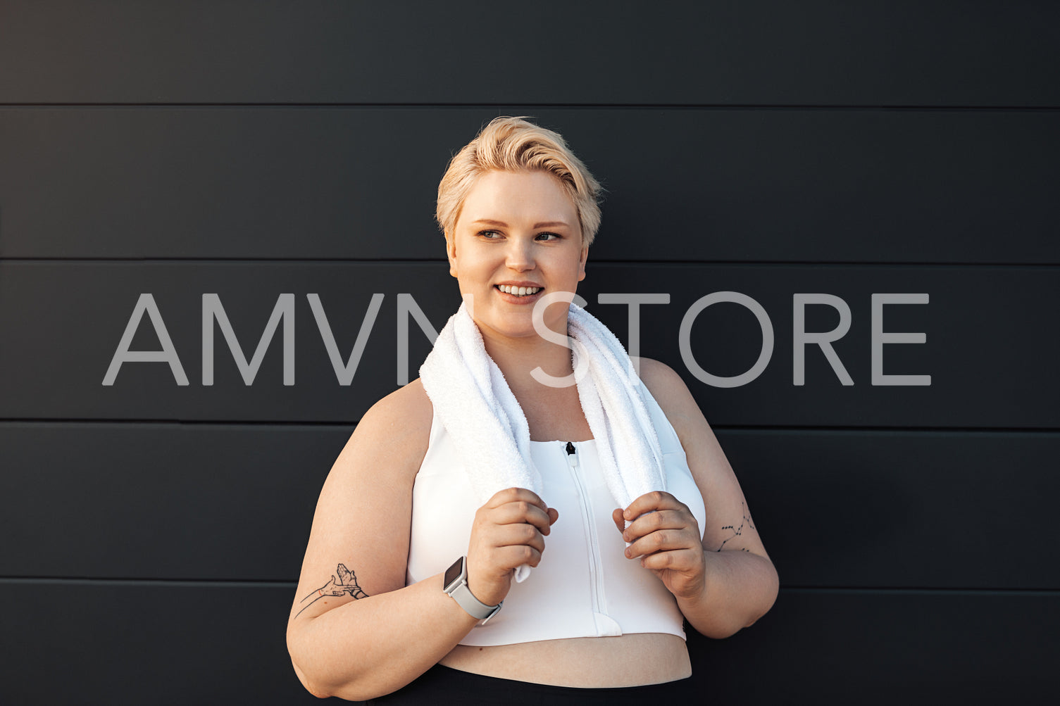 Portrait of a smiling woman in sportswear leaning on wall with a towel around her neck	