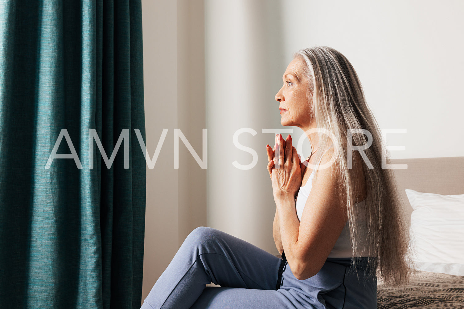 Side view of a senior woman with long hair looking thoughtful while sitting on a bed