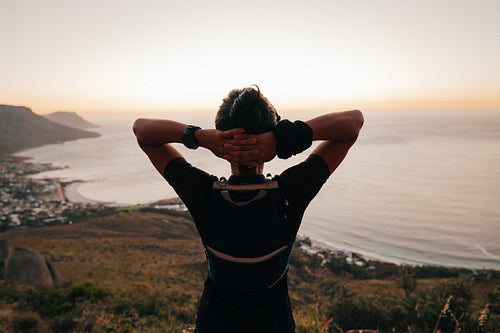 Rear view of sportswoman standing with his hands behind head and taking a break at sunset