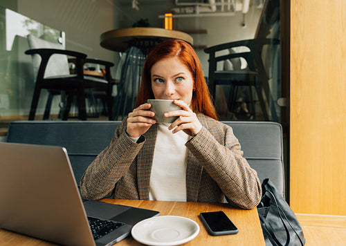 Businesswoman in a jacket holding a cup sitting at cafe in the morning