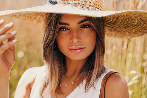 Beautiful woman in straw hat posing on a field and looking at camera