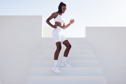 Full length of a young female practicing outdoors. Slim sportswoman jogging on stairs warming up before a workout.outdoors.