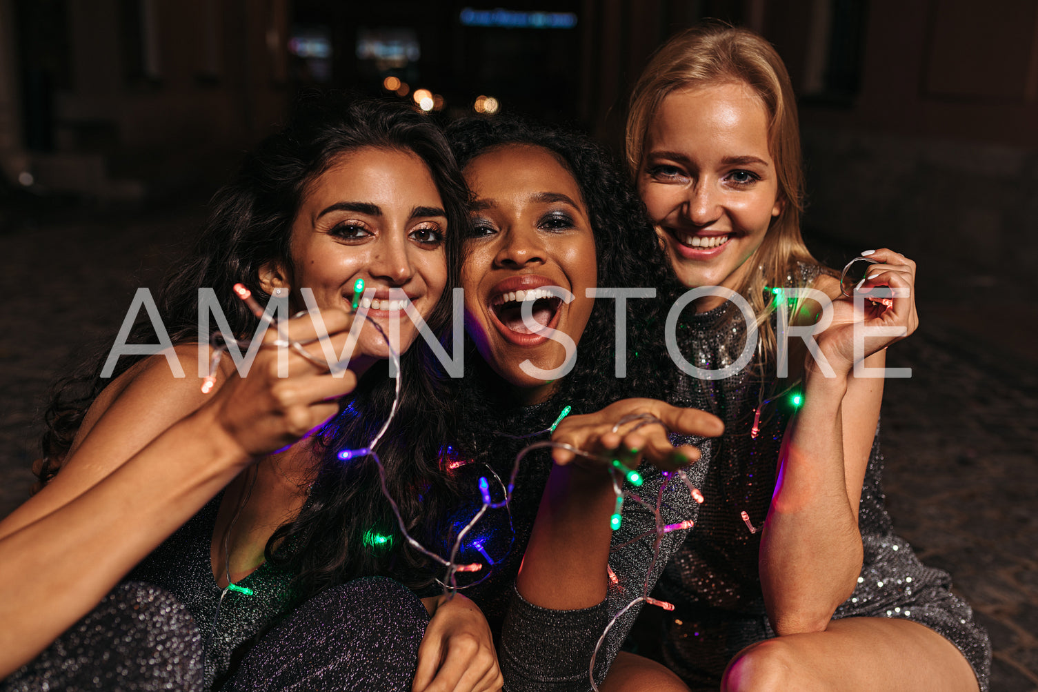 Happy women holding christmas lights in hands, sitting on sidewalk	