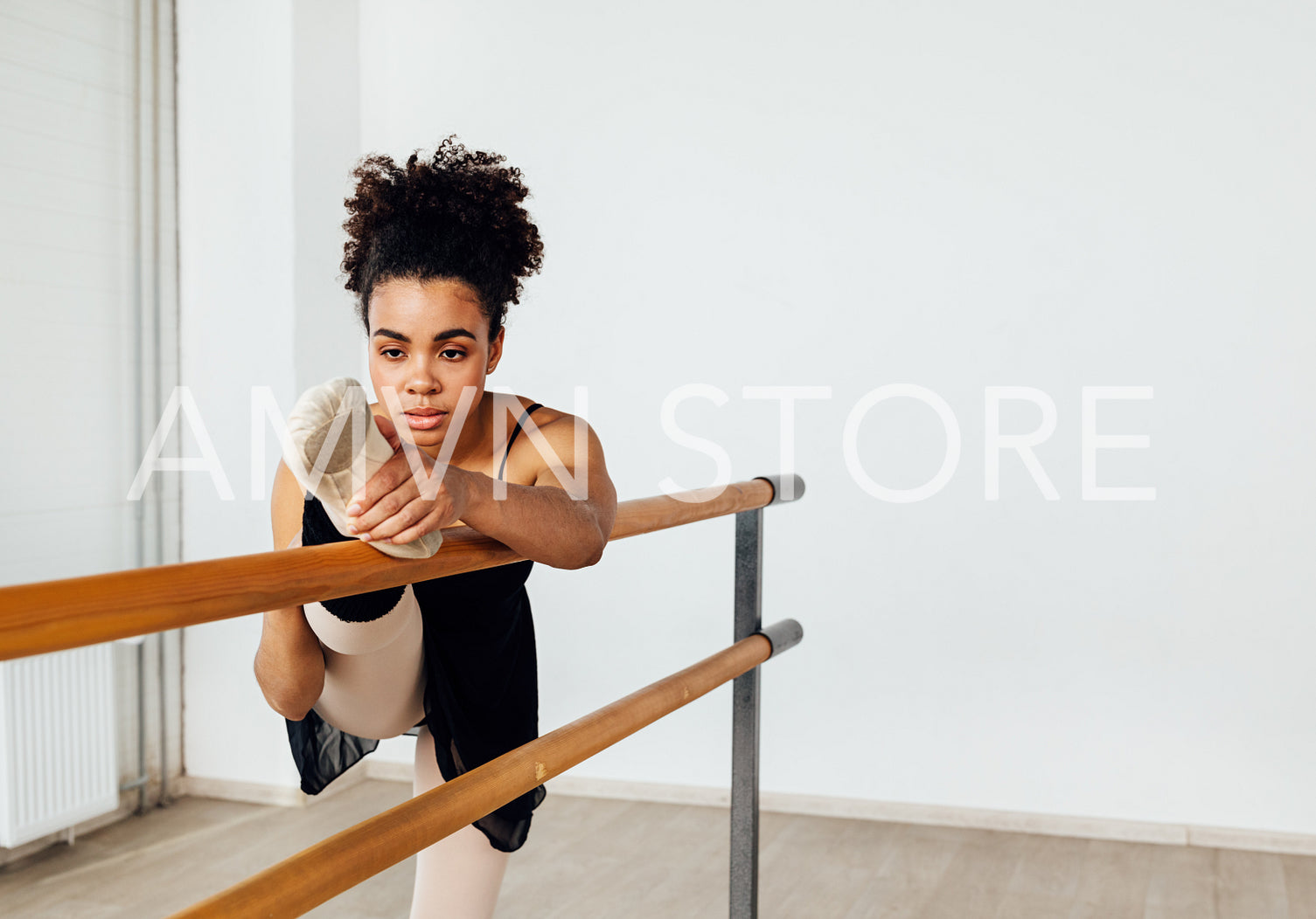 Ballerina stretching her leg on barre while practicing ballet dance in studio	