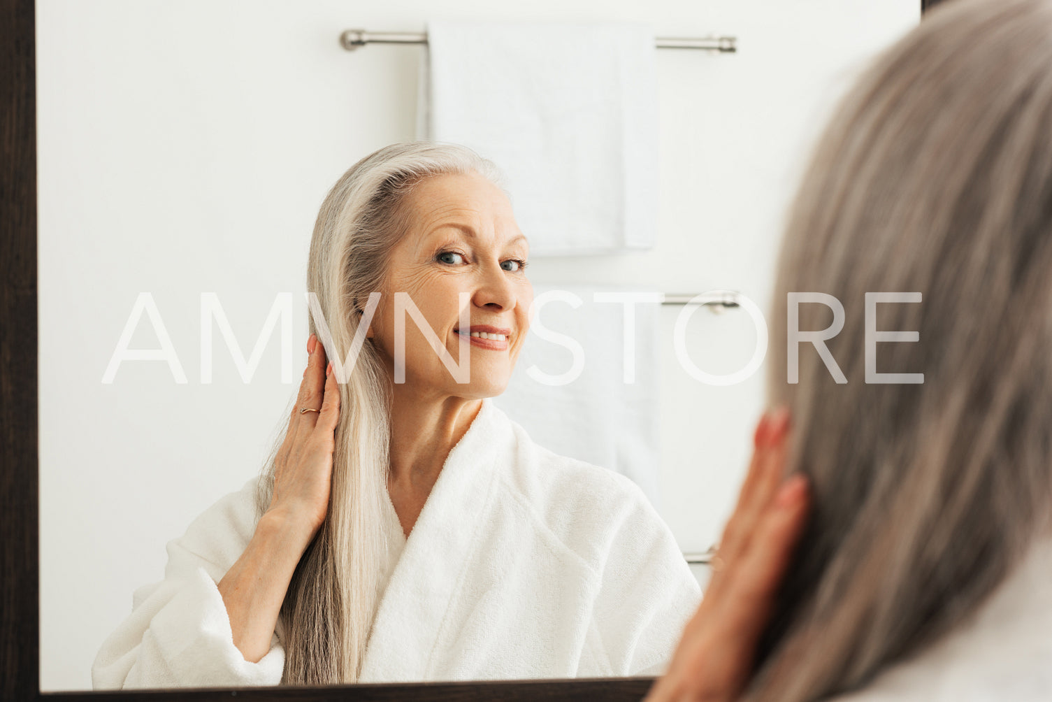 Senior woman touching her long grey hair and looking at a mirror in bathroom