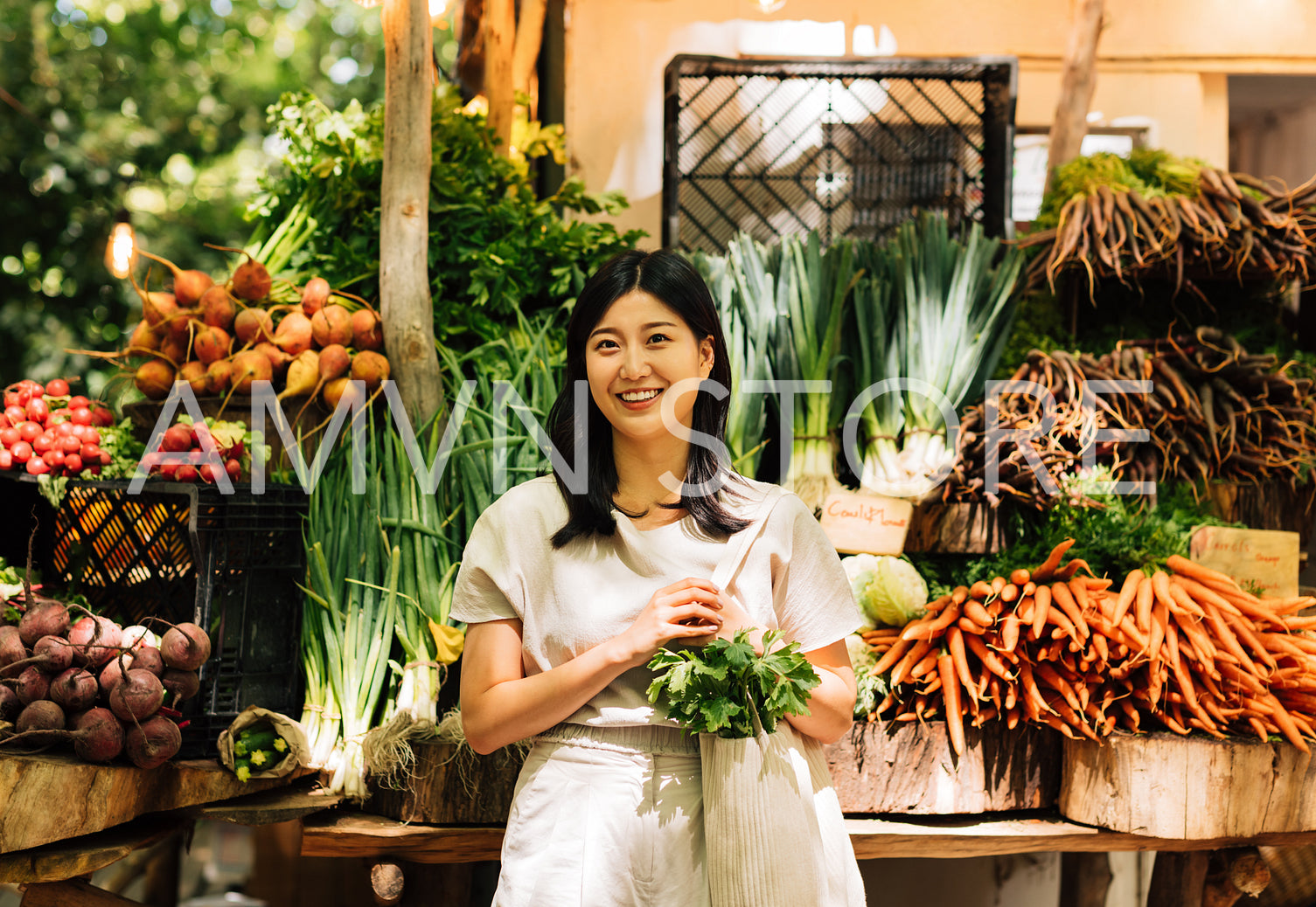 Cheerful Asian woman with a shopping bag standing at a farmers market. Young female standing at a stall in an outdoor market and looking at camera.