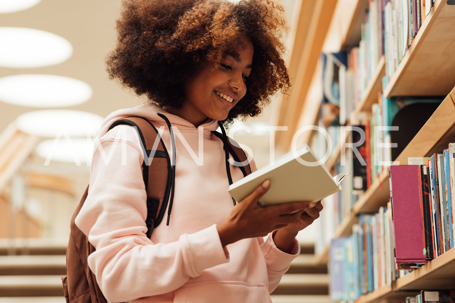 Smiling girl holding a book in library while standing at bookshelf