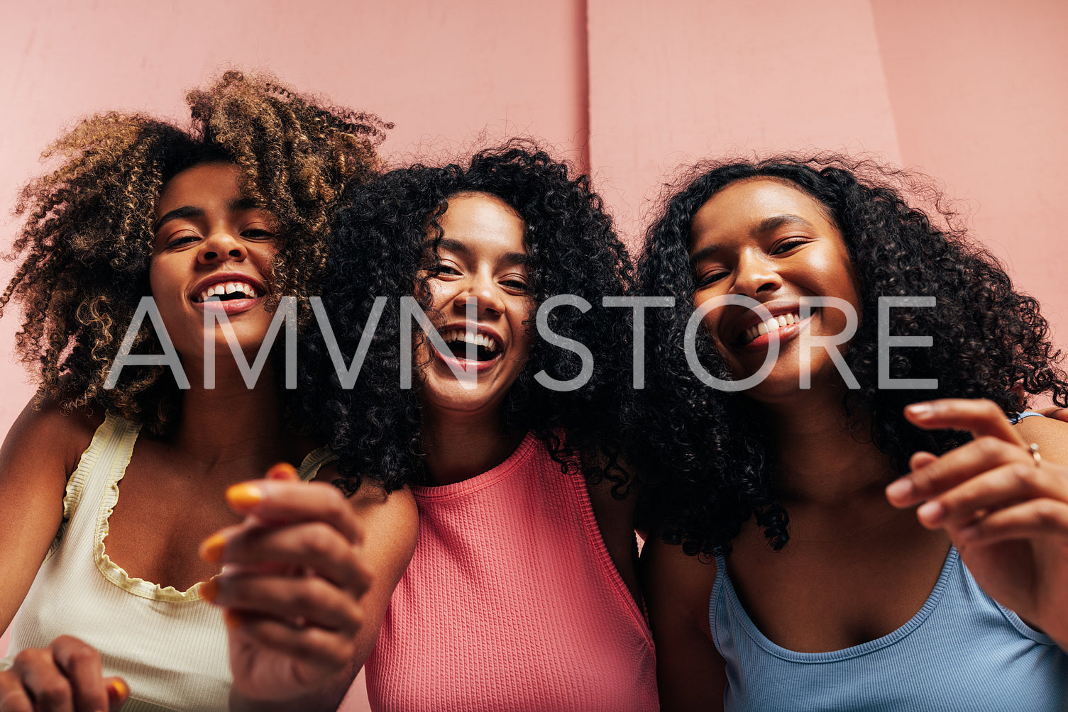 Three happy girlfriends with curly hair laughing together and looking at camera