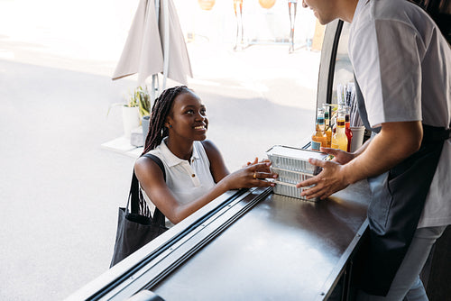 Smiling African American woman buying street food. Midsection of salesman holding takeaway packaged food.