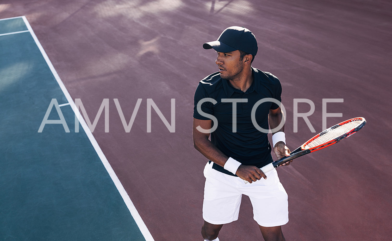 Tennis player in sportswear and a cap standing on a hard court preparing to receive the serve. Tennis player during a tennis match.