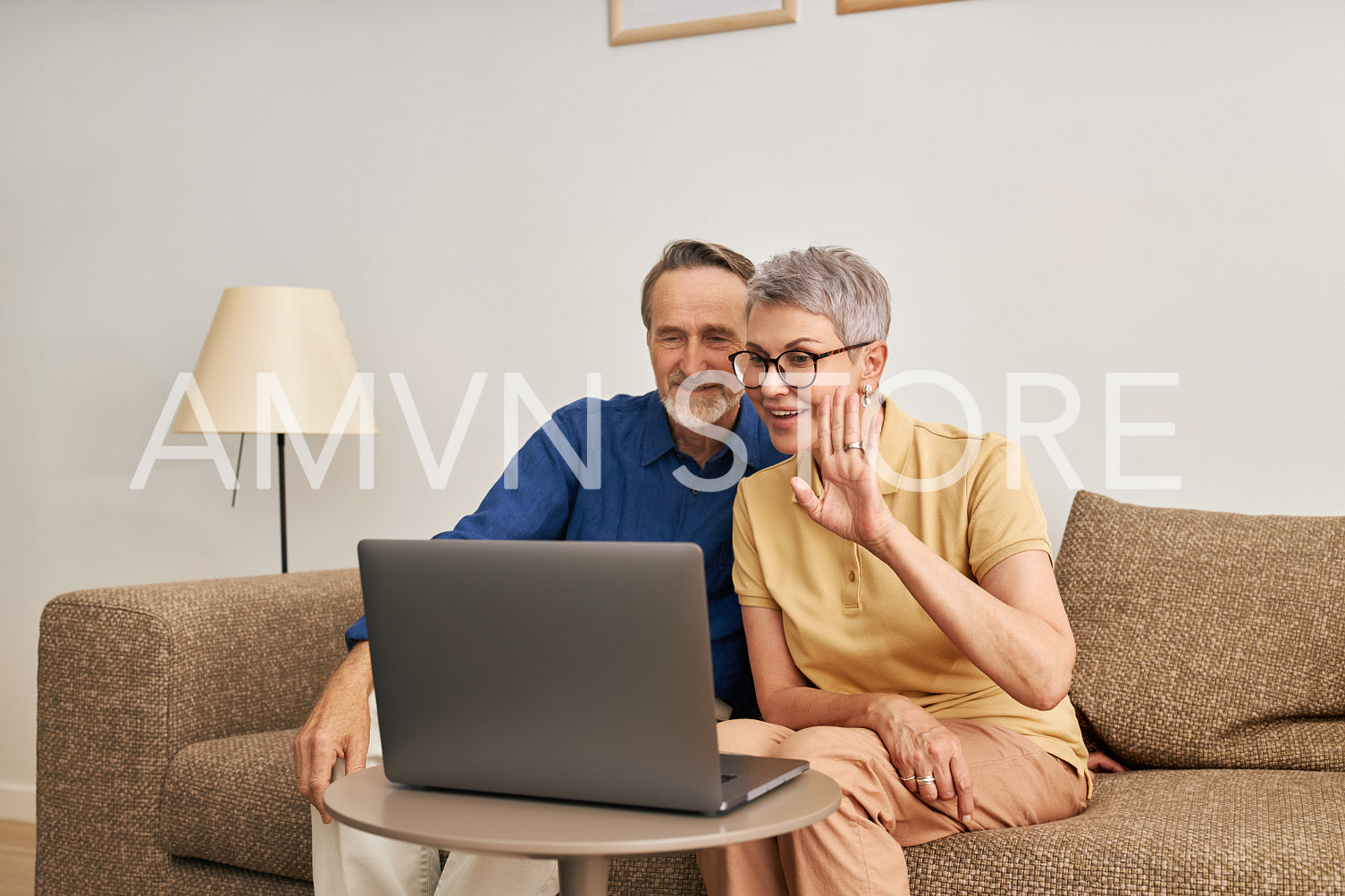 Cheerful senior couple using a laptop for video calling from the living room. Woman and man sitting	