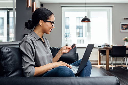 Side view of smiling woman holding a card using laptop on hips at home