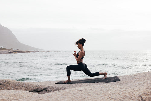 Woman in fitness wear practicing yoga on a mat at seashore