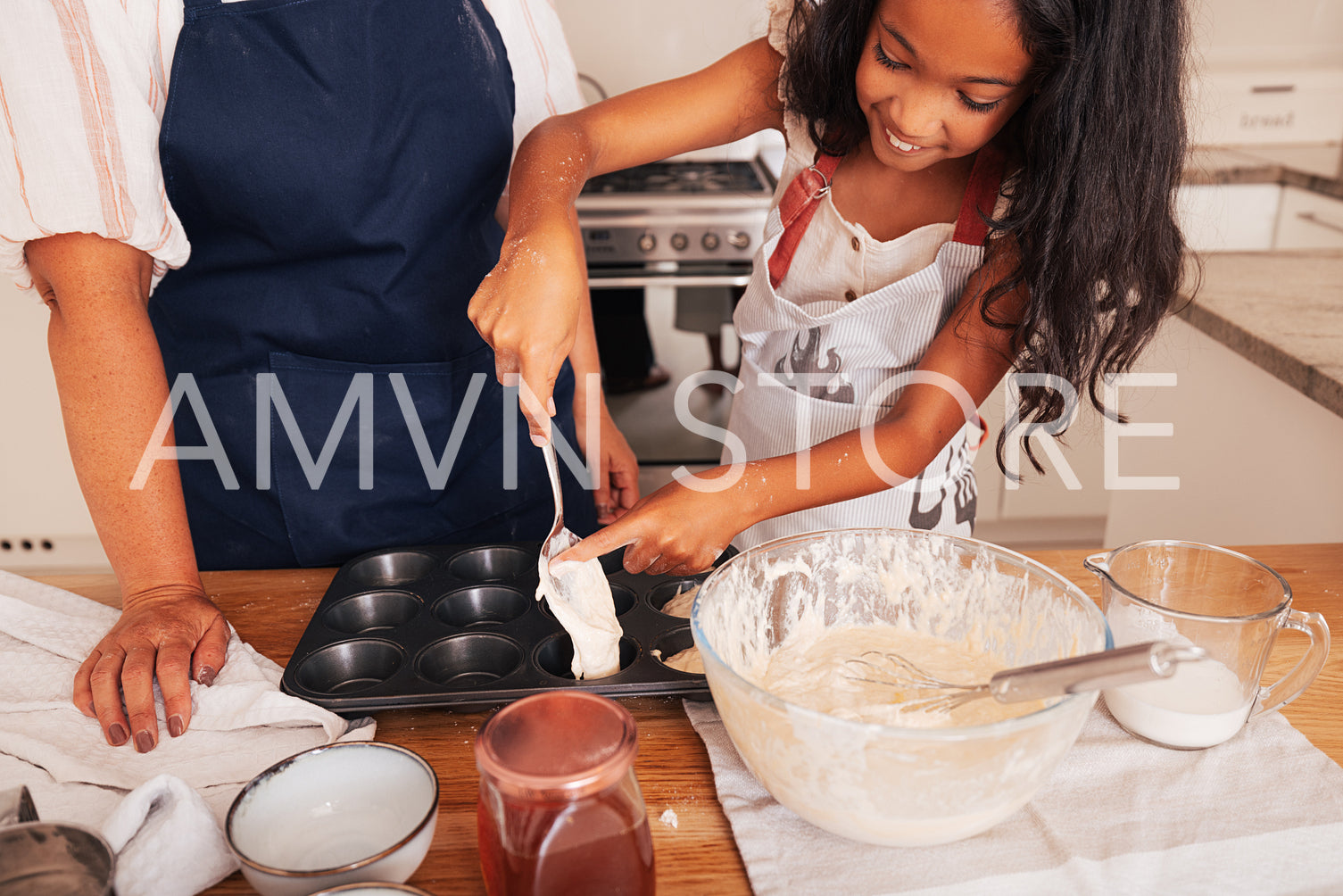 Smiling girl pouring batter from spoon and helping with her finger into cupcake moulds