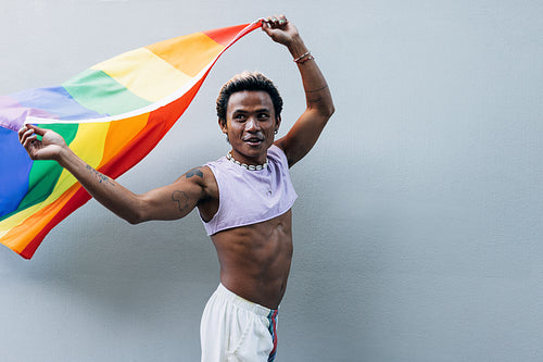 Young man holding rainbow flag at grey wall