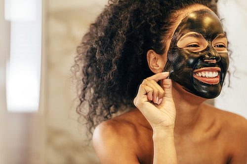 Smiling woman removing black cosmetic mask from her face