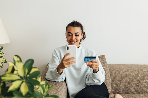 Smiling woman using smartphone and credit card. Young female making a purchase online.