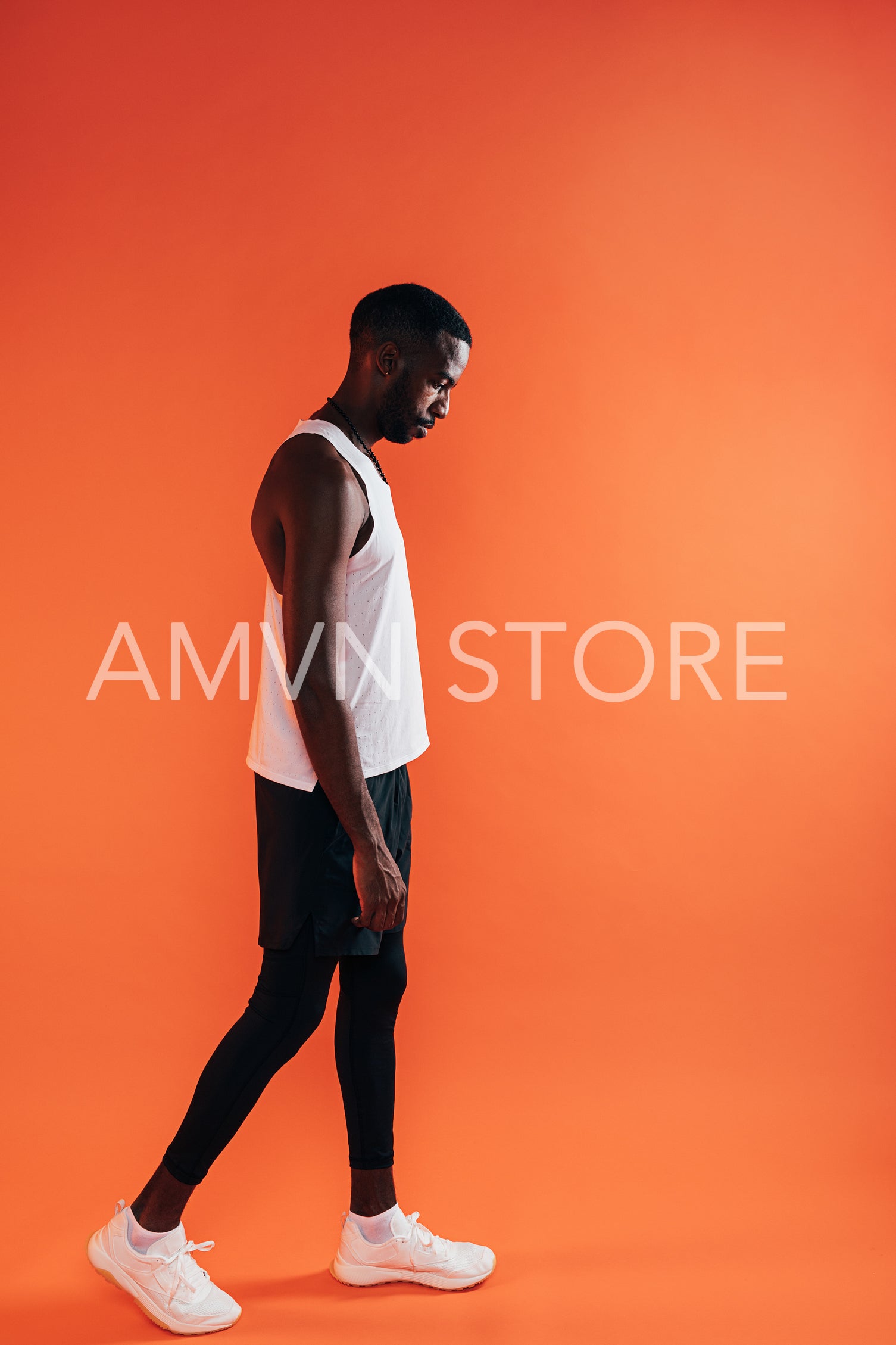 Side view of a man in sports clothes standing against an orange background and looking down