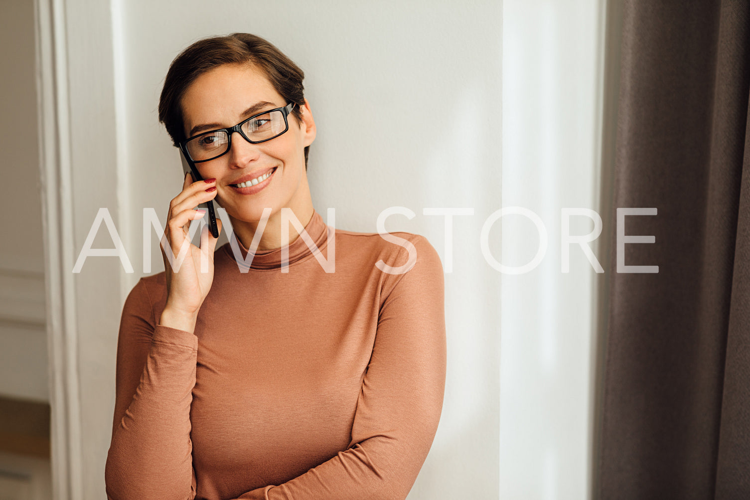 Smiling businesswoman using talking on a mobile phone while standing at the hotel room wall	