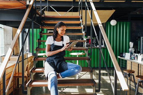 Coffee shop owner sitting on staircase and reviewing business files on digital tablet