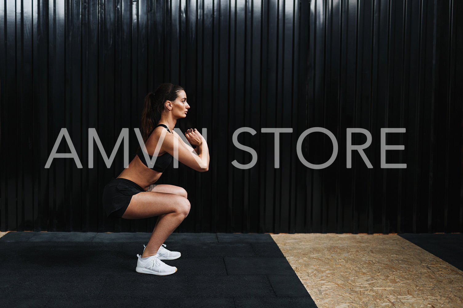 Side view of sporty woman practicing squat exercises in gym near black wall	