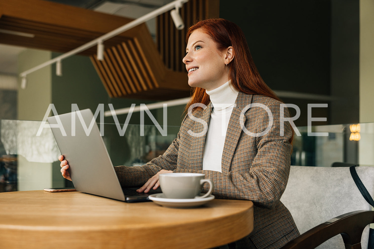 Woman entrepreneur sitting at a table with a laptop. Redhead female working remotely from a cafe.